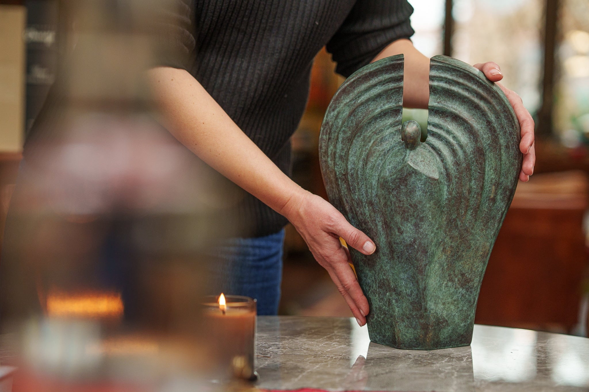 Person holding a green bronze urn angel on a table with a blurred background