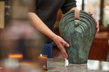 Person holding a green bronze urn angel on a table with a blurred background